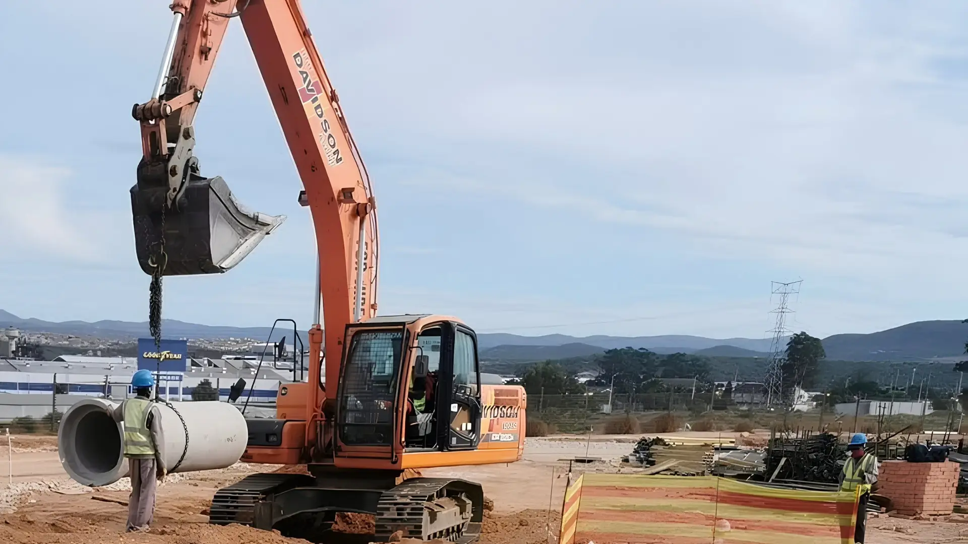 Excavator lifting a concrete pipe section on a civil construction site