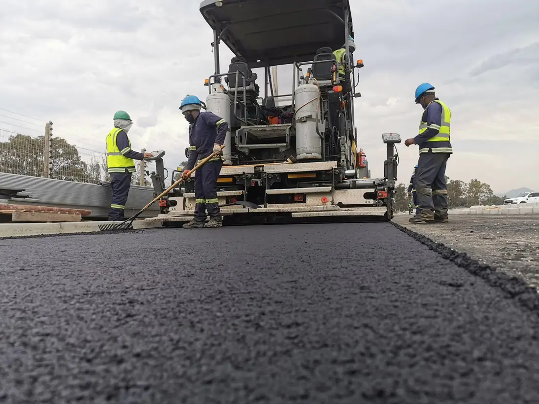 Asphalt paver laying a new road surface with the crew